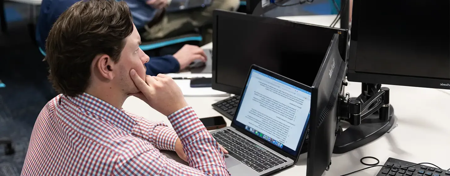 A group of individuals working at desks with computers, engaged in various tasks.